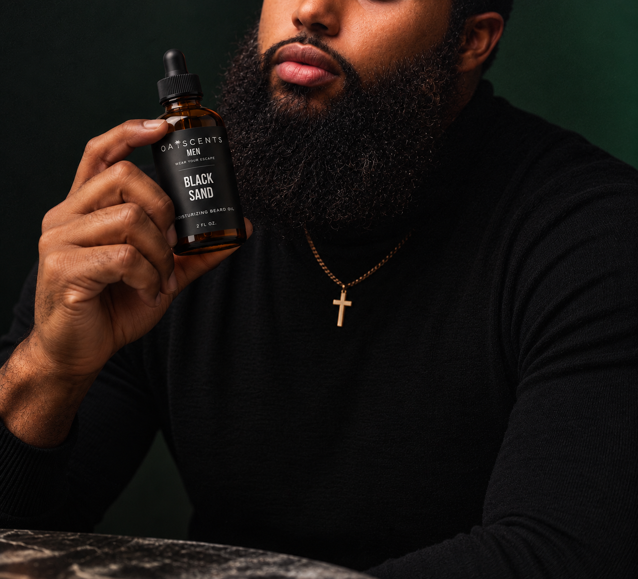 A man with a full beard in a black turtleneck and gold cross necklace holding a bottle of Oaiscents Black Sand Moisturizing Beard Oil against a deep green backdrop