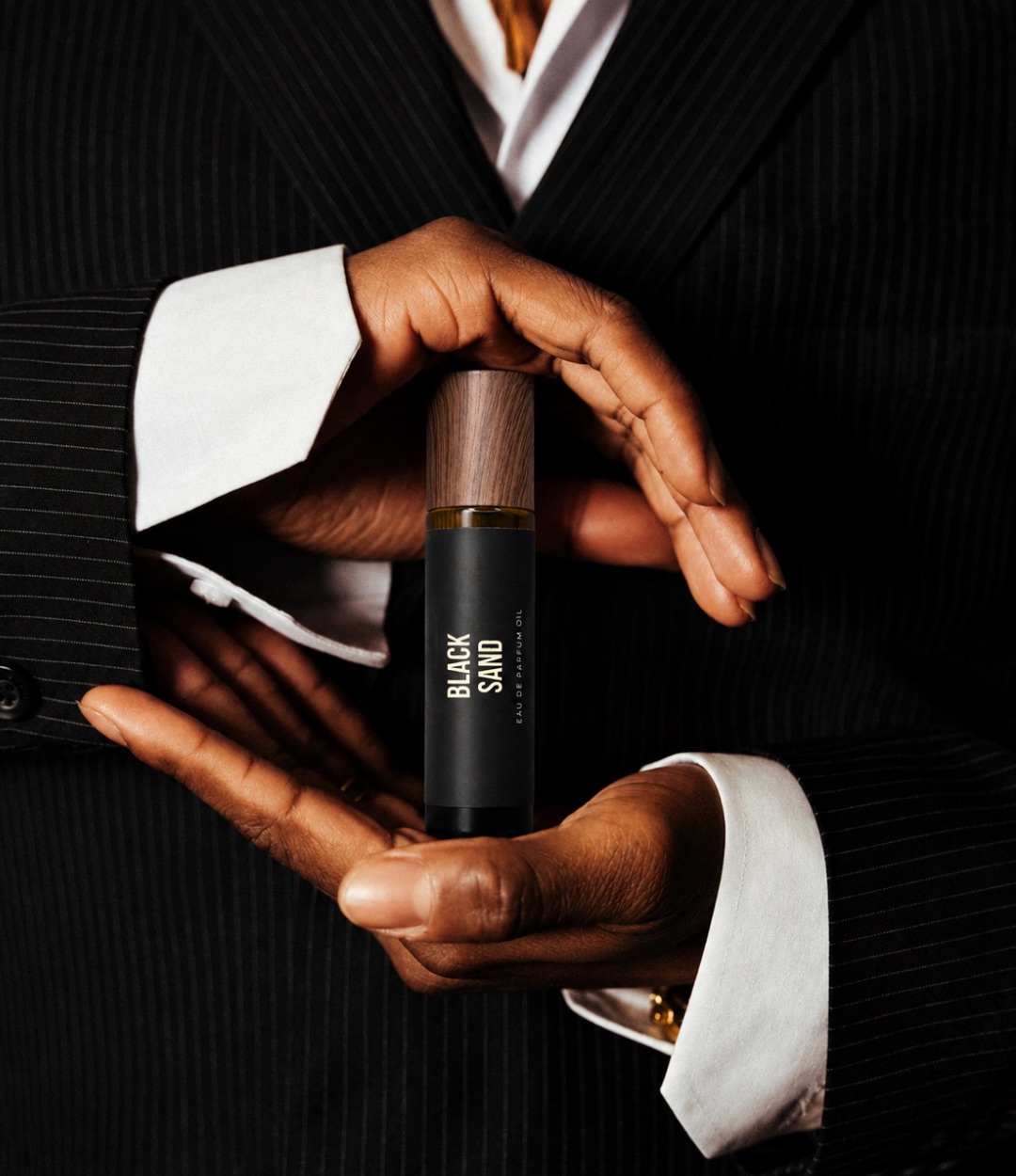 Black Sand held between the hands of a man in a pinstripe suit